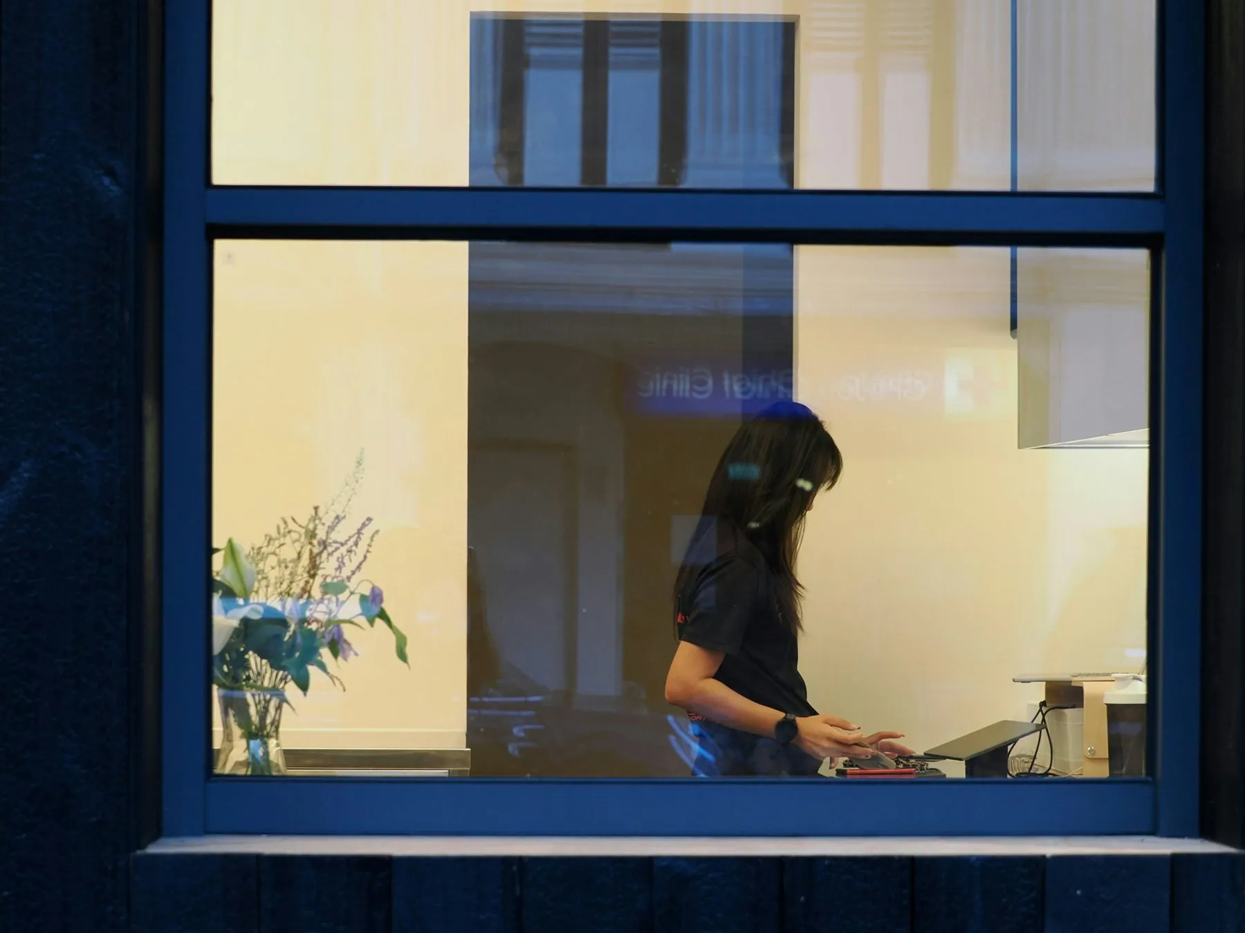 A woman works inside a room, viewed through a window