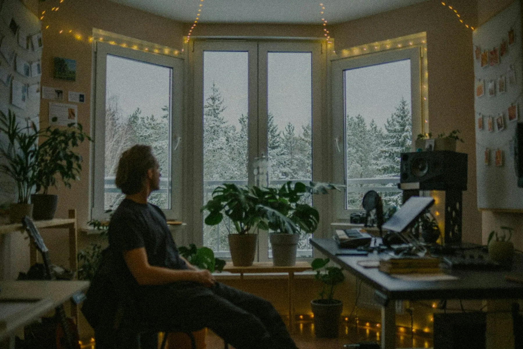 Man looking out window at snowy trees from cozy room