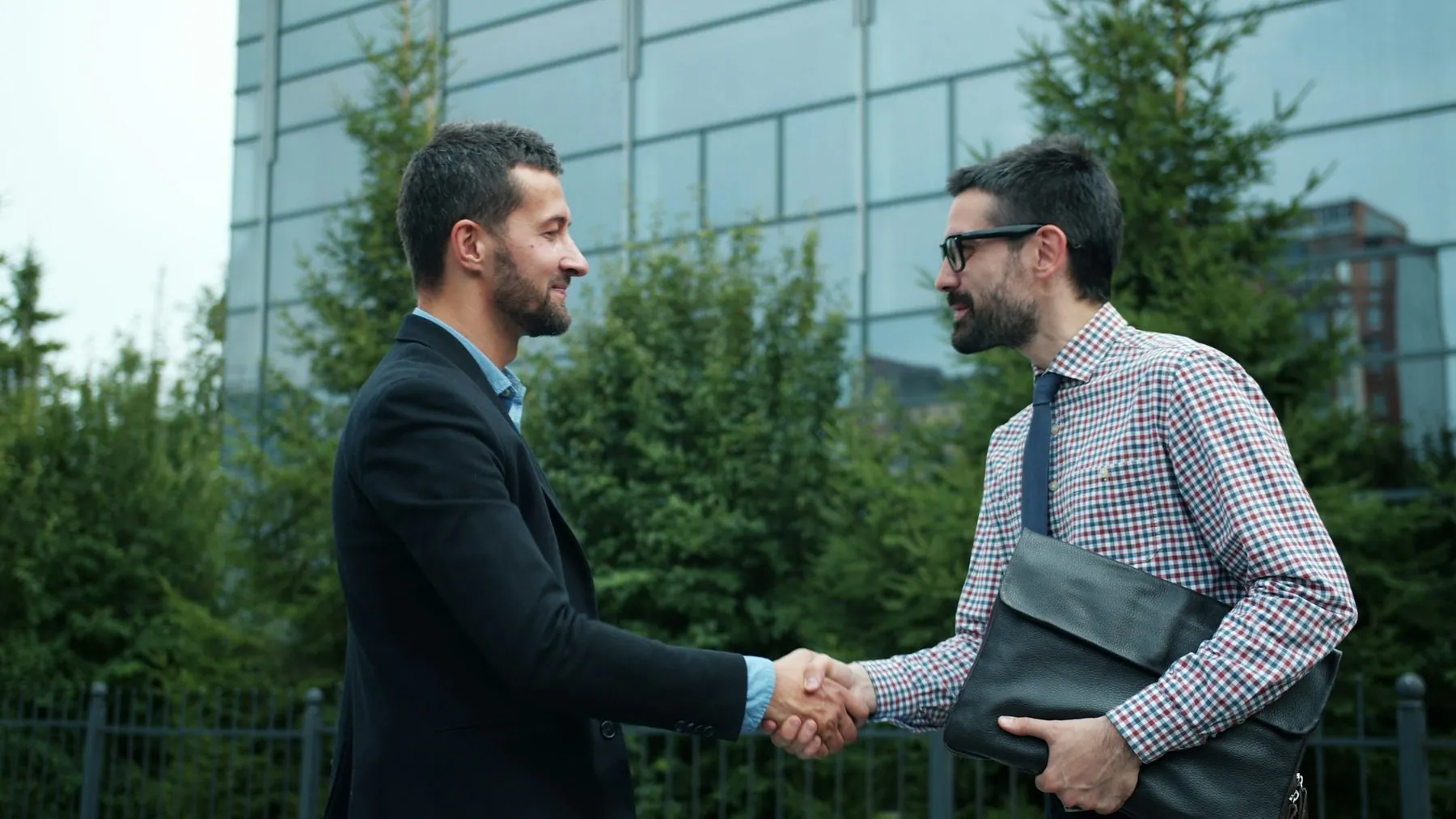 Business partners handsome young men are meeting outdoors in city shaking hands greeting saying hello enjoying partnersh