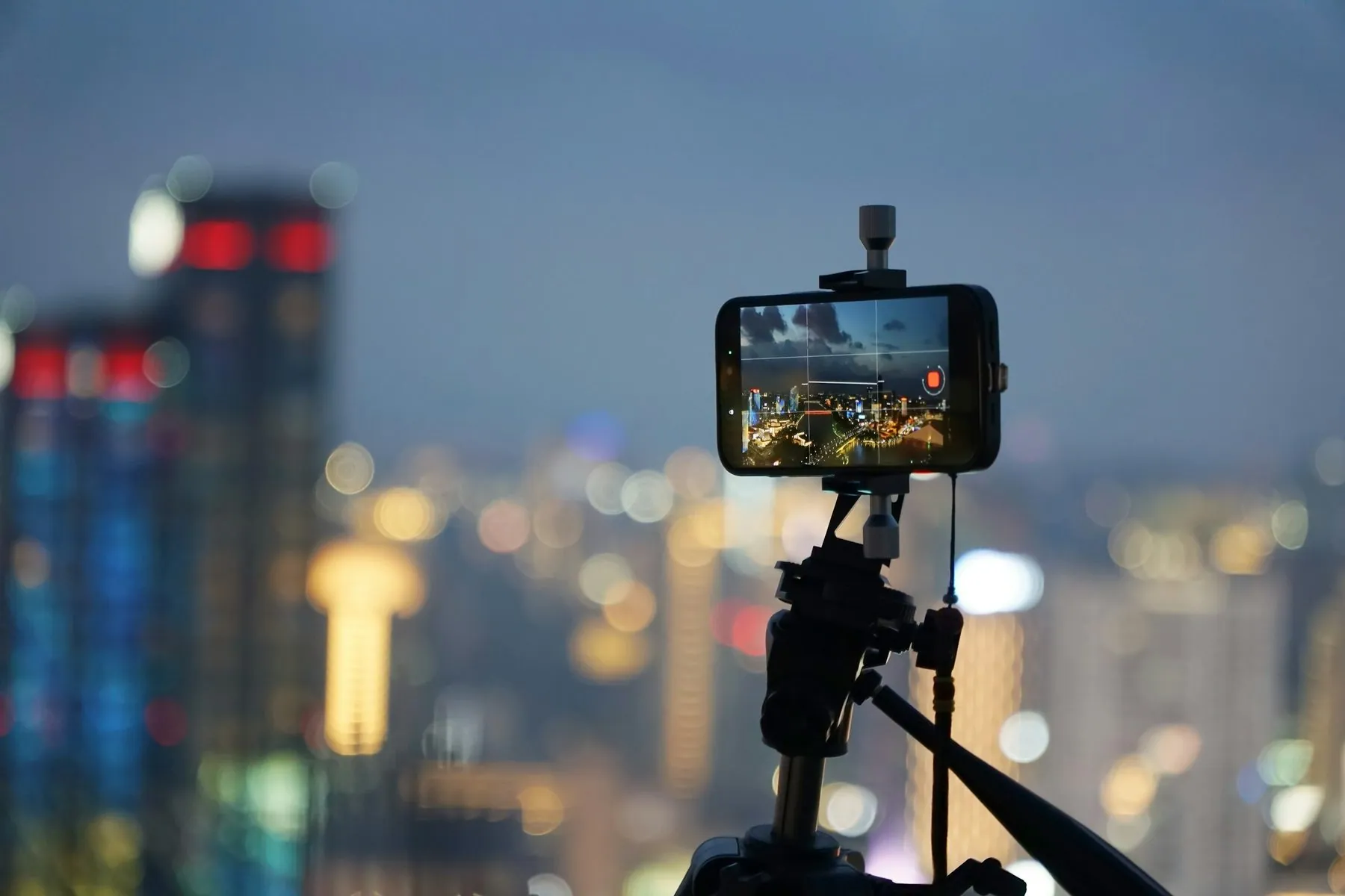 A smartphone on a tripod recording a city skyline with bokeh lights at night