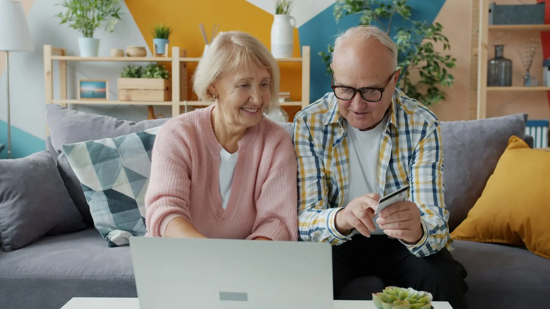 Cheerful elderly people man and woman are making cashless online payment with bank card using laptop at home. Money, ret
