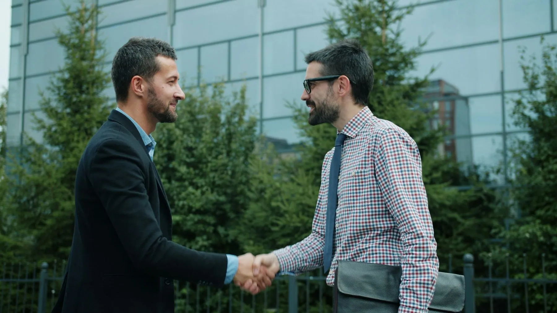 Businessmen handsome ambitious guys in formalwear are meeting outdoors shaking hands smiling ready for partnership. Gree