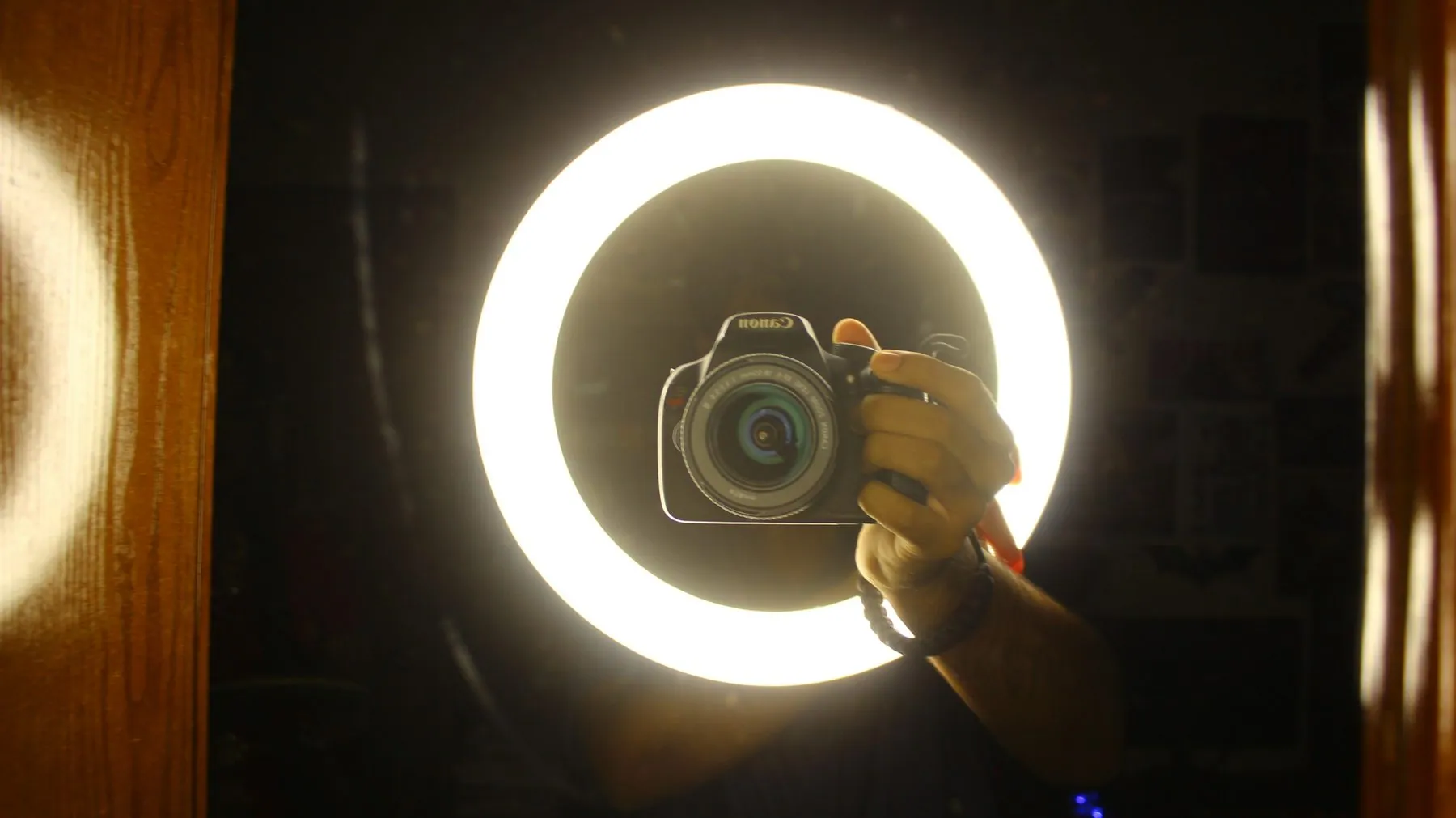 A person holding a camera in front of a bright circular ring light