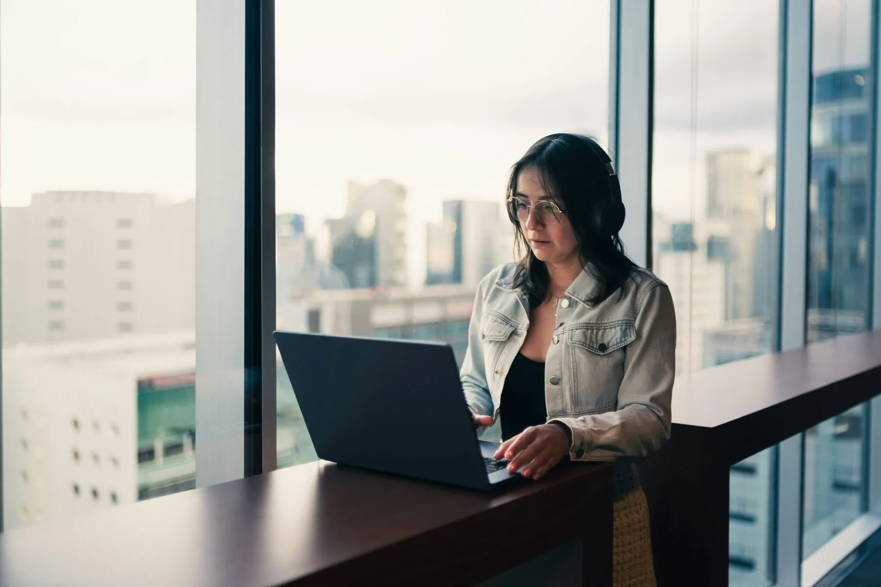 Woman wearing headphones working on a laptop by window