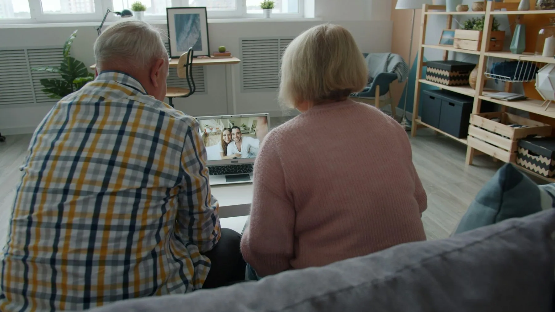 Cheerful elderly people are talking to happy young couple making online video call with laptop at home communicating to
