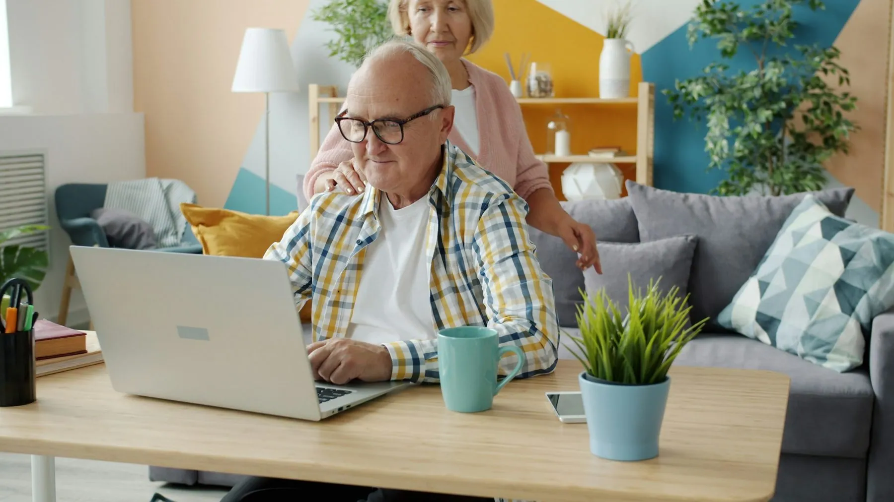 senior man using laptop working while wife hugging talking looking at screen. Modern technology, people and relationship