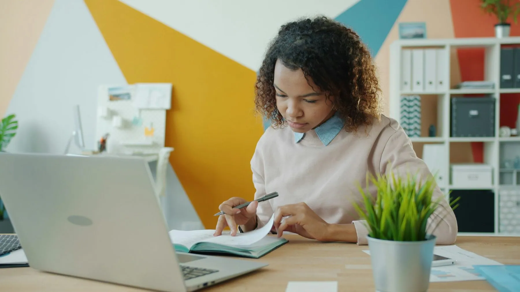 Serious young Afro-American woman is writing in notebook working in office alone concentrated on business information. P