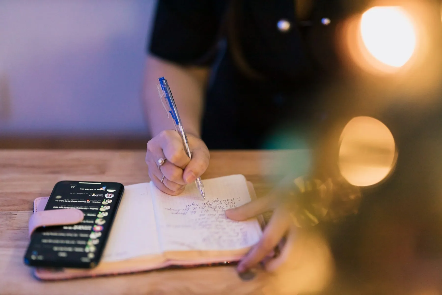 a person writing on a notebook with a cell phone