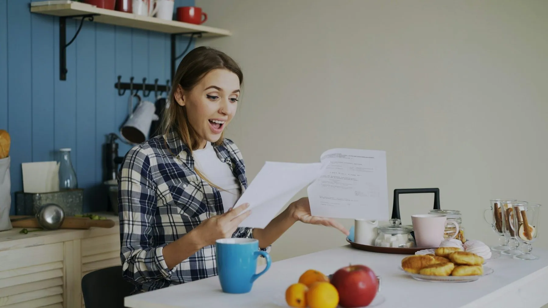 Young happy woman surprised to recieve good news reading letter in the kitchen while have breakfast at home