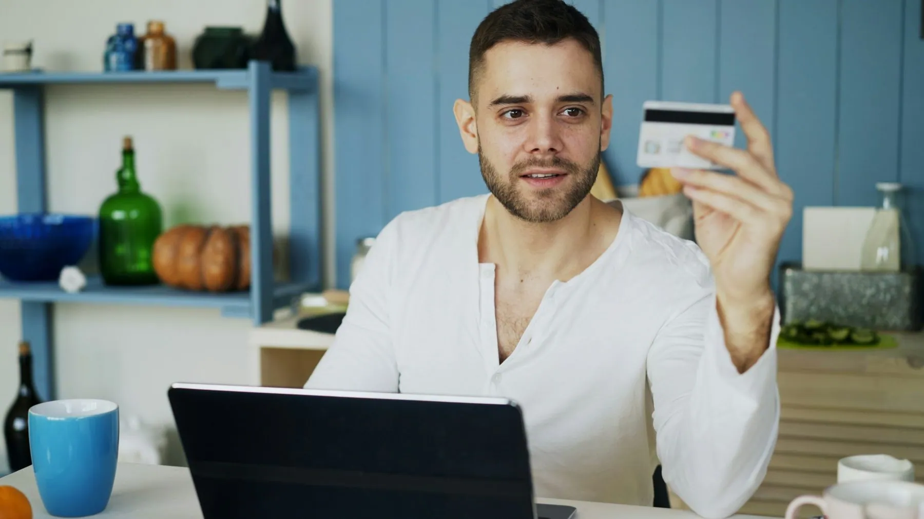 Young man having online shopping using credit card and laptop computer while have breakfast in the kitchen at home in th