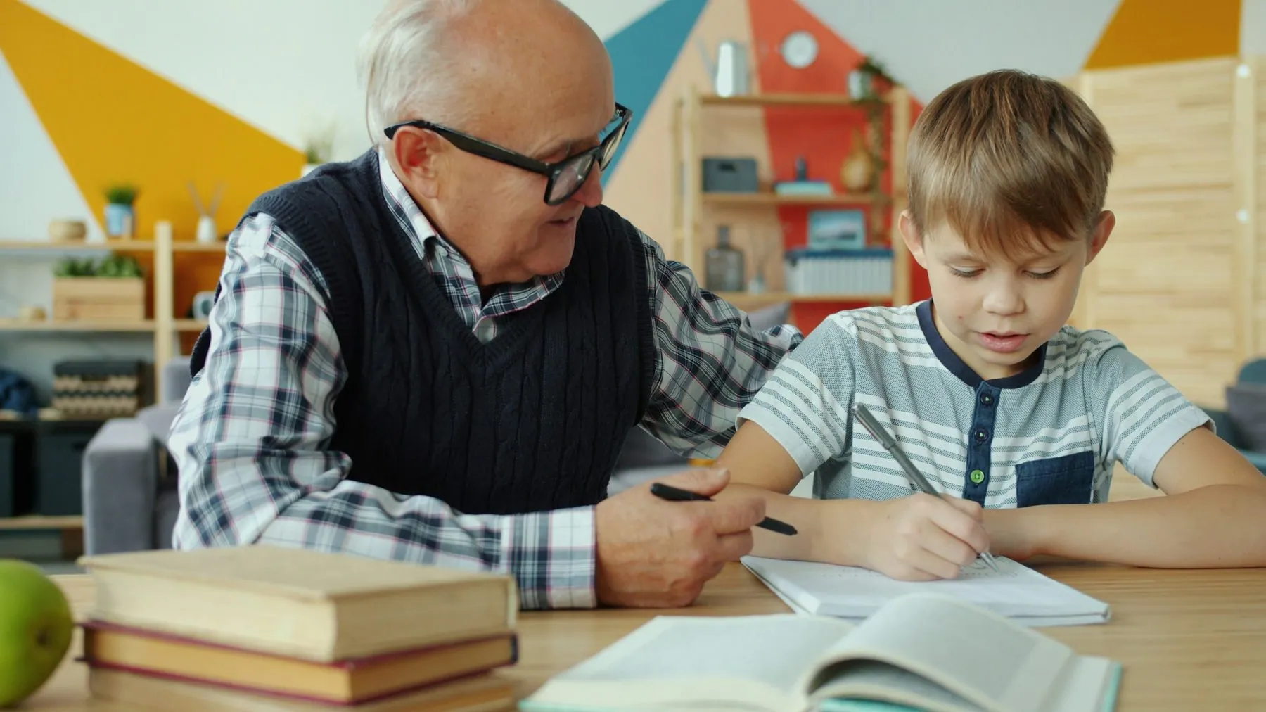 Grandfather senior man is helping junior boy child with homework talking sitting at desk together. Modern education, lov