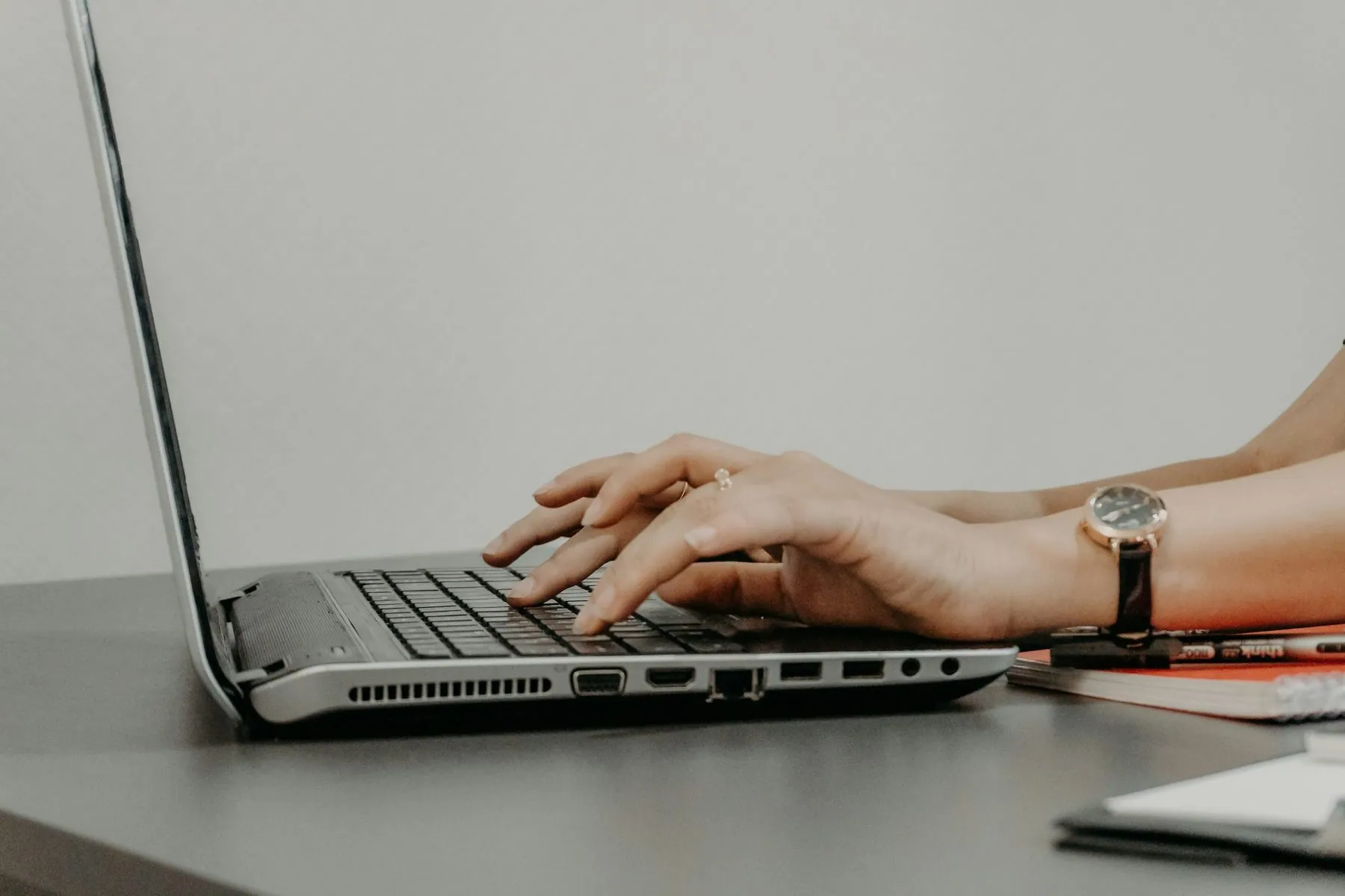 Hands typing on a laptop keyboard with a watch