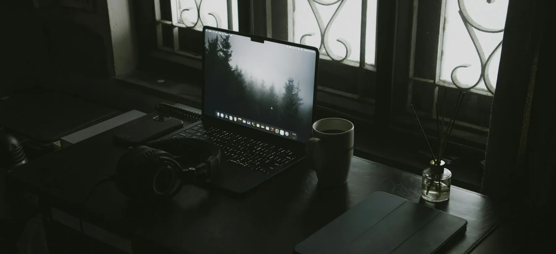 Desk with laptop, headphones, and coffee cup near window