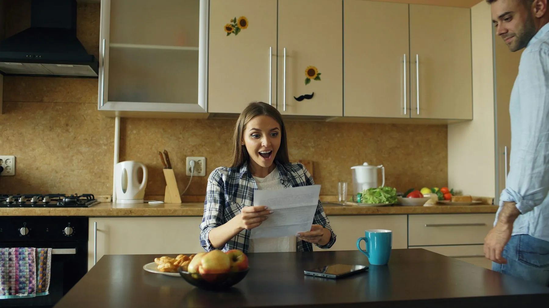 Attractive happy couple recieve good news unfolding letter in the kitchen while have breakfast at home early morning