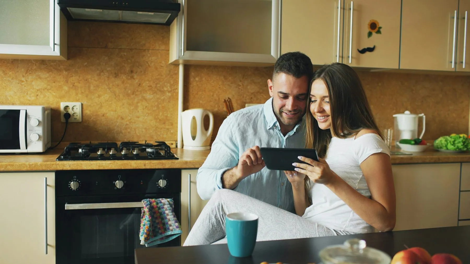 Happy young couple using digital tablet computer while sitting in the kitchen and having breakfast in the morning at hom