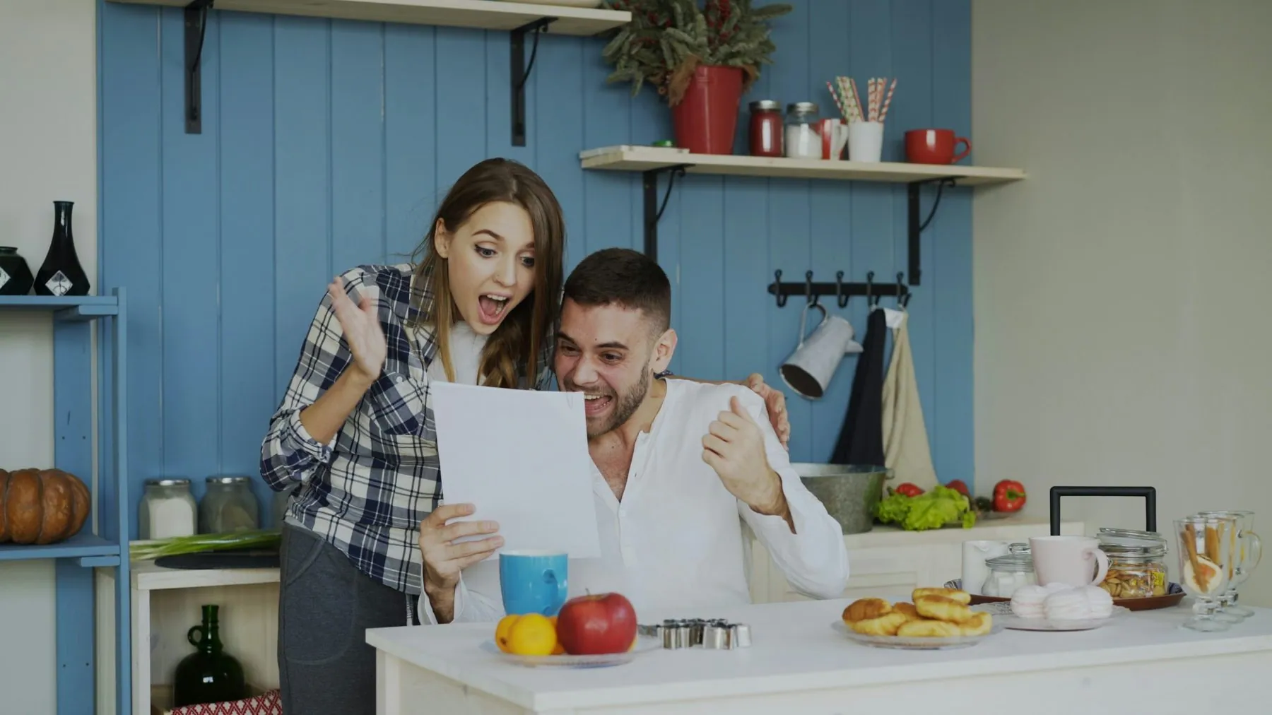Attractive happy couple recieve good news unfolding letter in the kitchen while have breakfast at home early morning