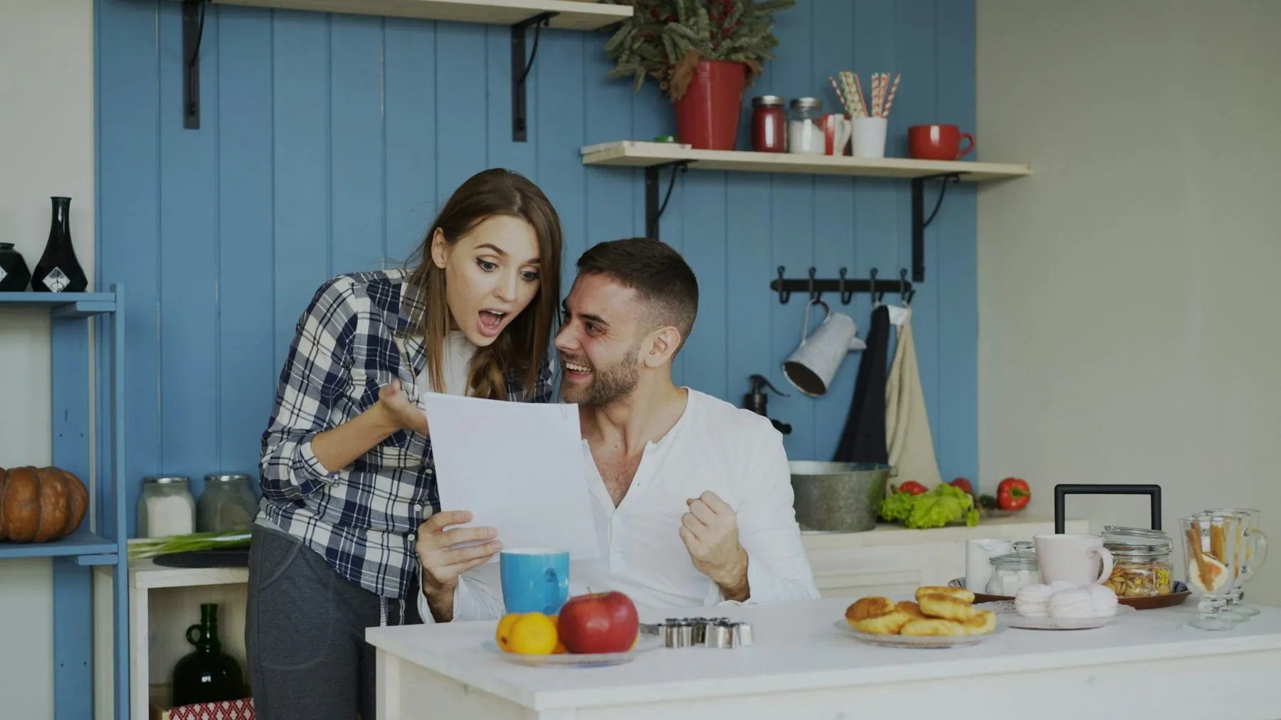 Attractive happy couple recieve good news unfolding letter in the kitchen while have breakfast at home early morning