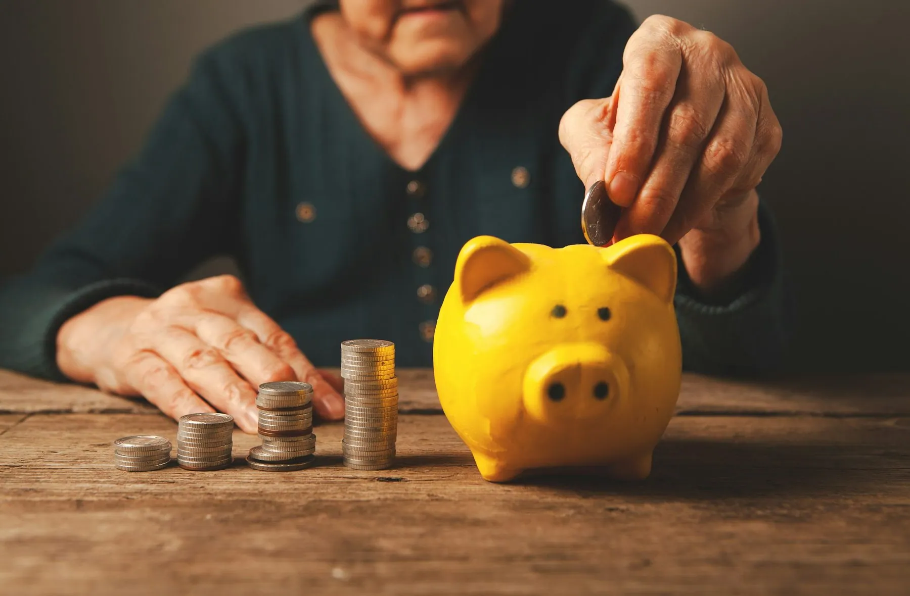 Elderly woman putting coin into a piggy bank. Retirement savings.