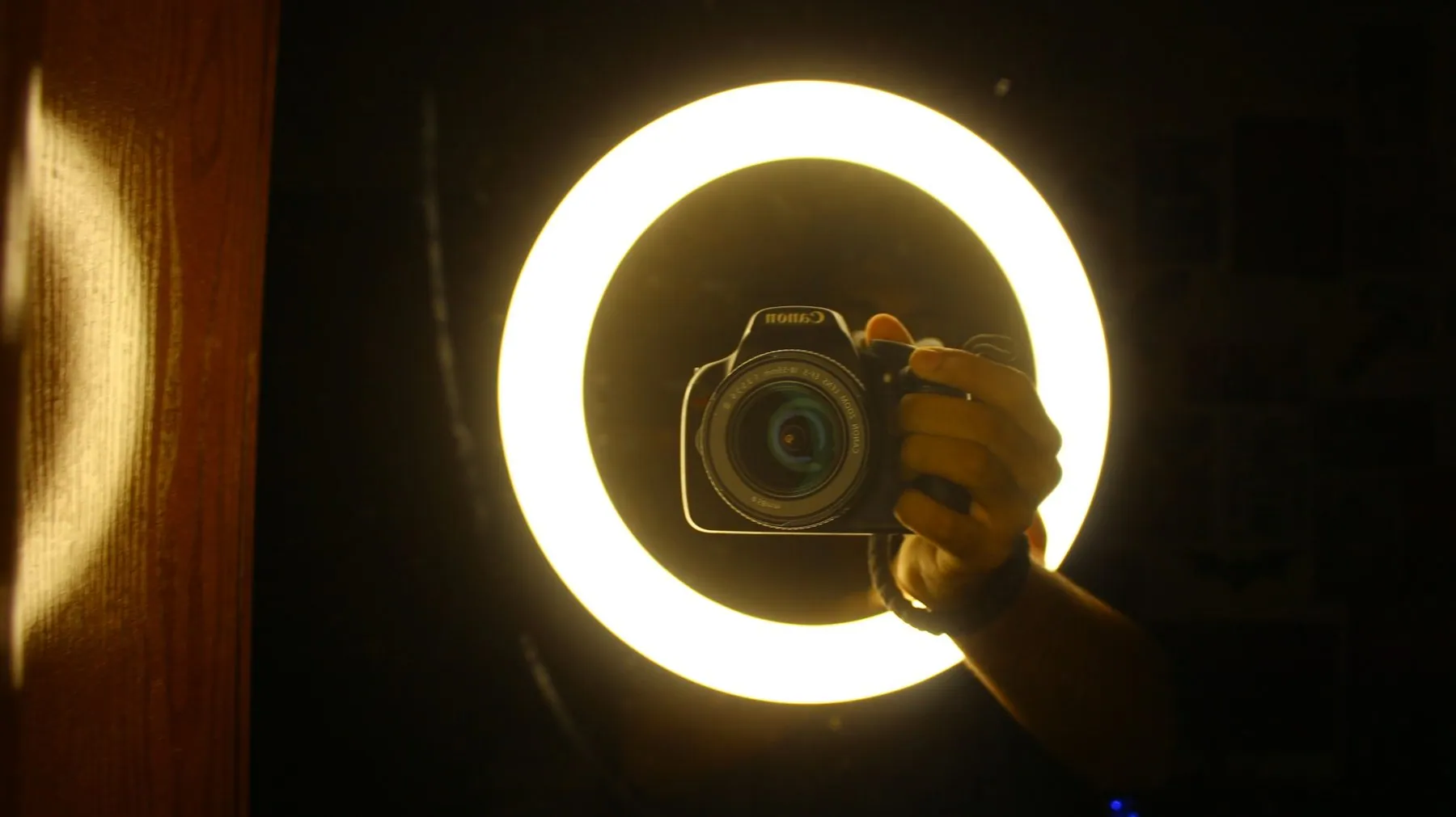 A person holding a camera in front of a bright circular ring light