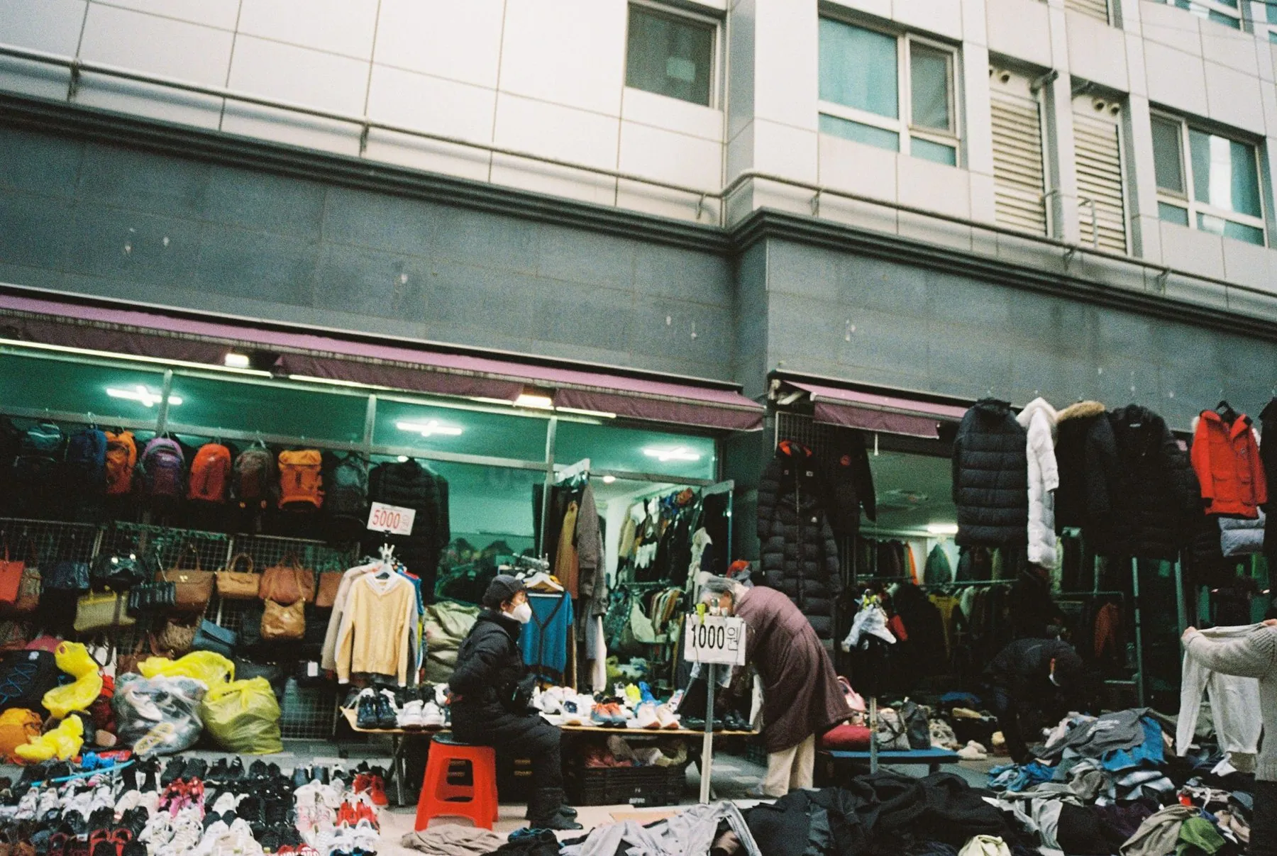 People browsing clothing and shoes at an outdoor market stall in a city