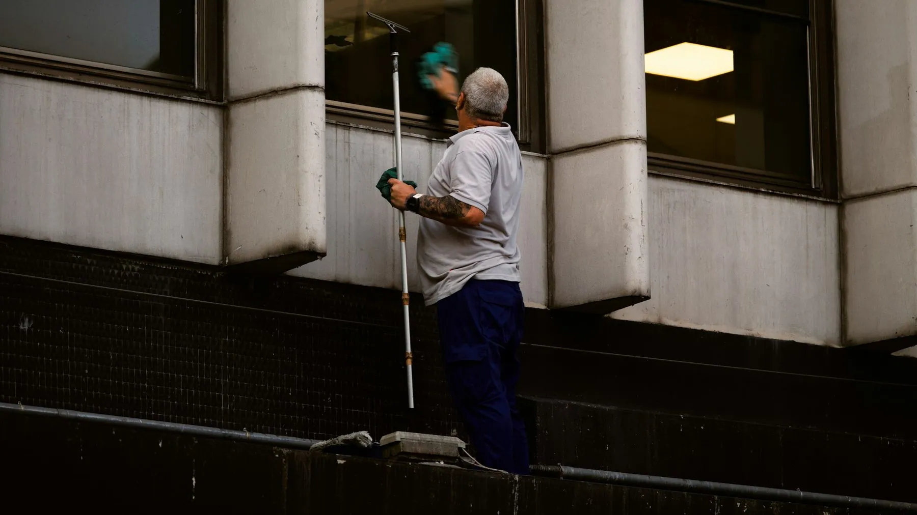 A person cleaning a window with a long squeegee on a building exterior