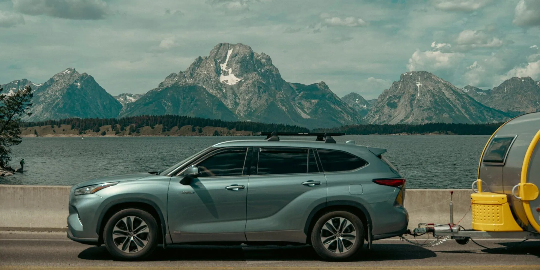 Suv towing a trailer with mountains and lake background