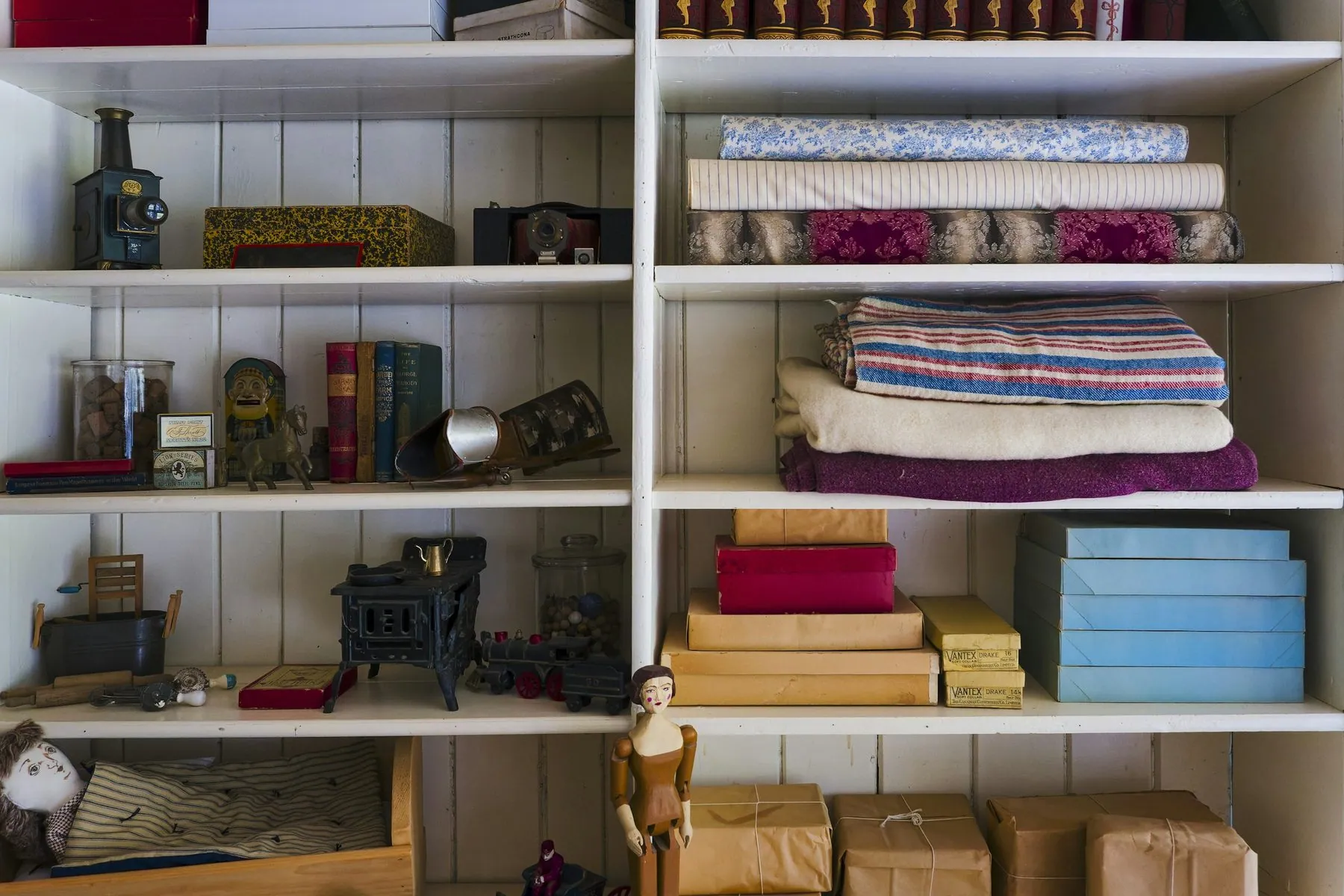 White Wooden Bookshelf Filled With Assorted Items in a Room - The image shows a white wooden bookshelf with five shelves