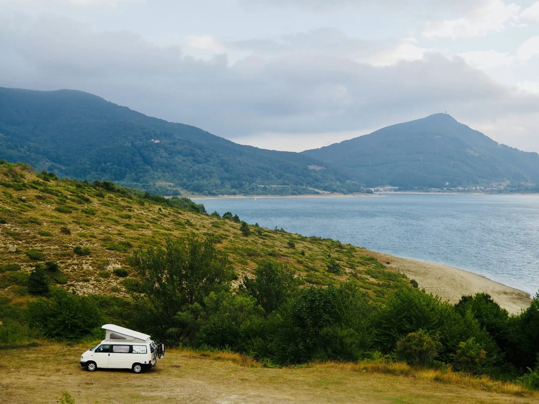 Camper van parked by a calm lake with rolling hills